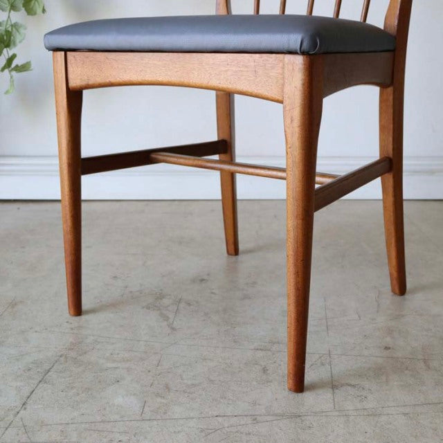Vintage mid-century teak dining chair with sharp back, black cushioned seat, and slender tapered legs from British Denmark.