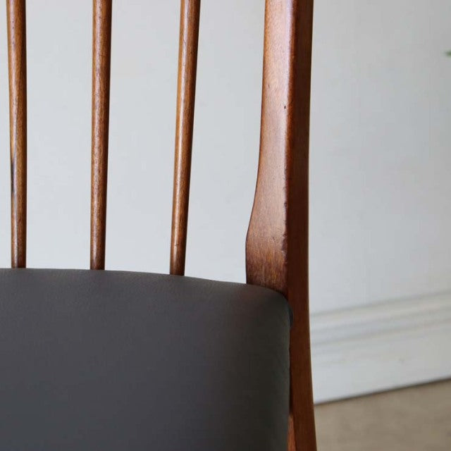 Vintage teak dining chair backrest with slim vertical spindles, mid-century British design, smooth wood grain, clean lines.