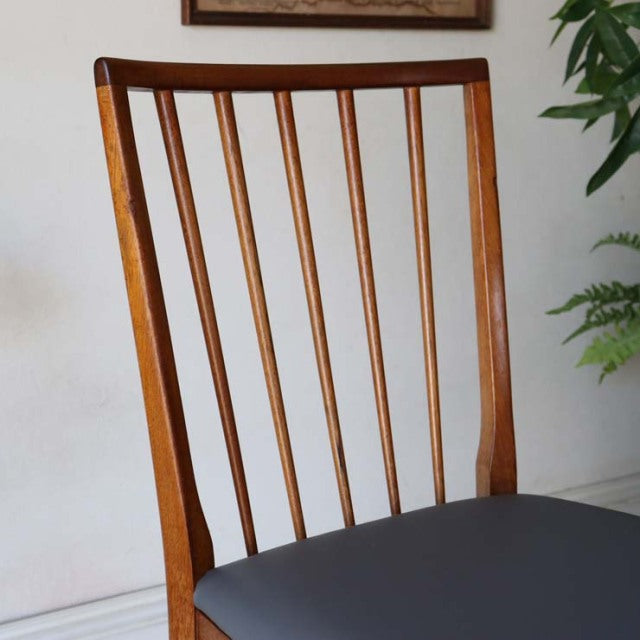 Mid-century British vintage teak dining chair with sharp backrest, vertical spindle slats, and dark upholstered seat.