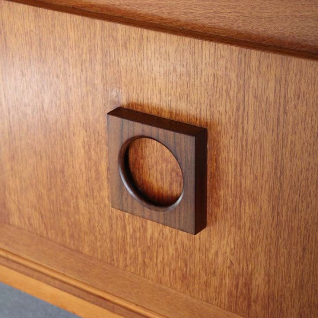 Close-up of vintage British mid-century teak sideboard featuring square wooden handle with circular cutout and warm wood.