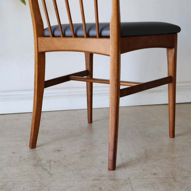 Set of four vintage British mid-century teak dining chairs with slender legs, curved spindled backs, and black upholstered.