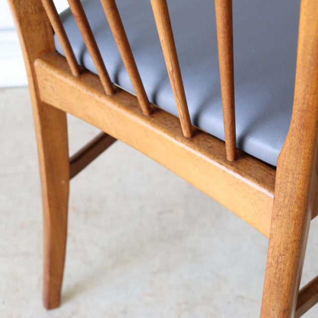 Mid-century British teak dining chair with sharp back spindles and dark upholstered seat, showcasing warm wood grain and.