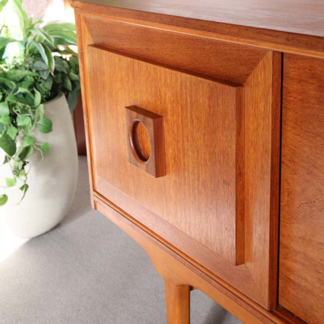 Vintage teak mid-century British sideboard with sculpted wood grain panel and circular recessed handle on slender tapered.