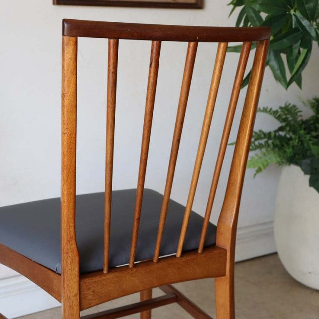 Vintage teak mid-century British dining chair with vertical spindle back and sleek black seat cushion.