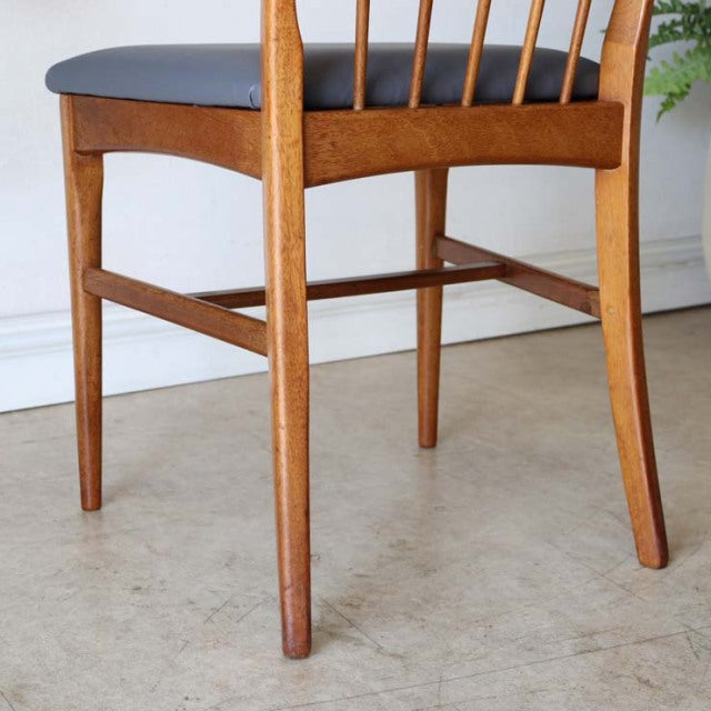 Vintage teak dining chair with sharp backrest, tapered legs, and black leather seat, mid-century British-Denmark style.