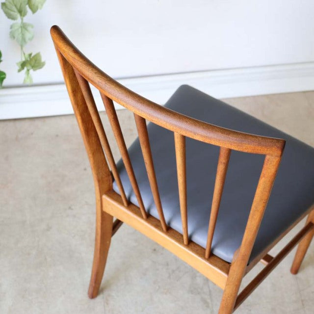 Vintage mid-century British teak dining chair with slender vertical spindle back and black cushioned seat, showcasing warm.