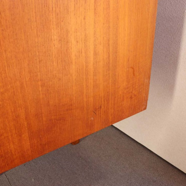 Mid-century British vintage teak sideboard corner showing warm wood grain and slender tapered leg detail in natural light.