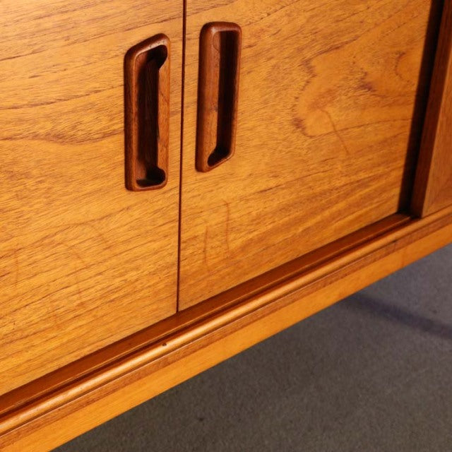 Close-up of vintage teak mid-century British sideboard doors with recessed handles and visible wood grain, Danish design.