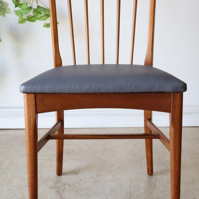 Vintage mid-century teak dining chair with sharp back spindles, British-Denmark design, dark cushioned seat, visible wood.