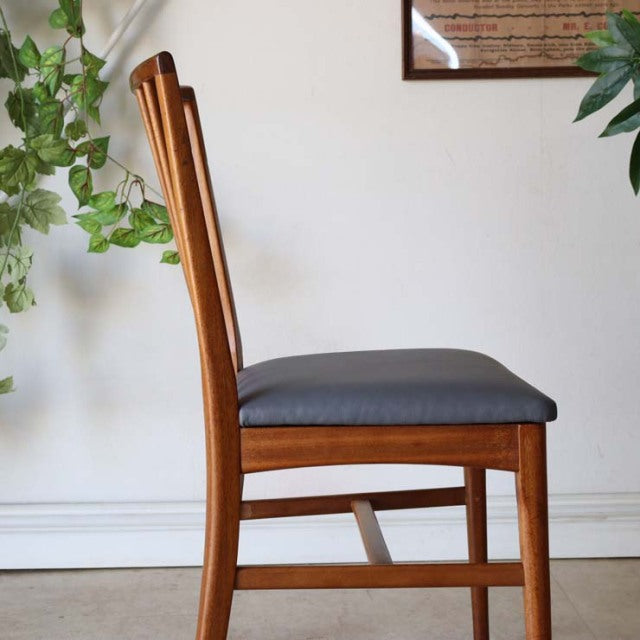 Vintage mid-century teak dining chair with sharp backrest, black seat cushion, and slender legs, British-Denmark design.