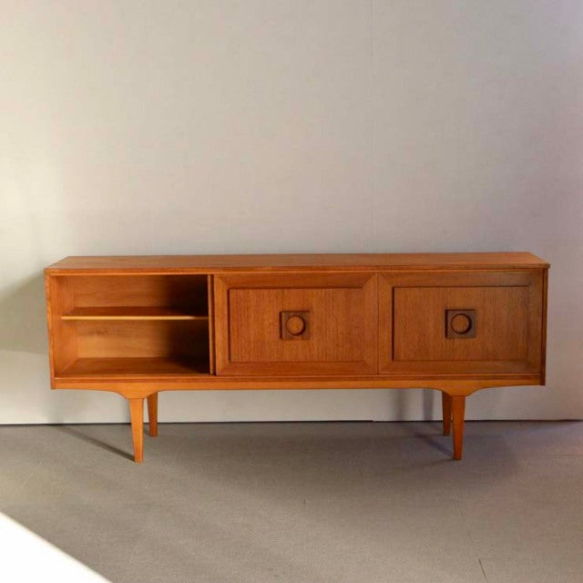 Mid-century vintage British teak sideboard with rich wood grain, tapered legs, two paneled doors, and open shelving on left.