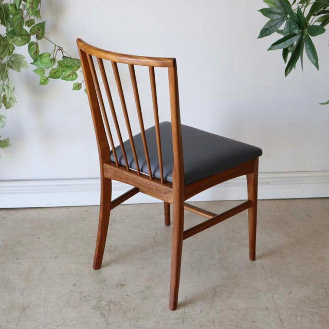 Vintage mid-century teak dining chair from Britain with vertical slat back and black cushioned seat, smooth wood grain.