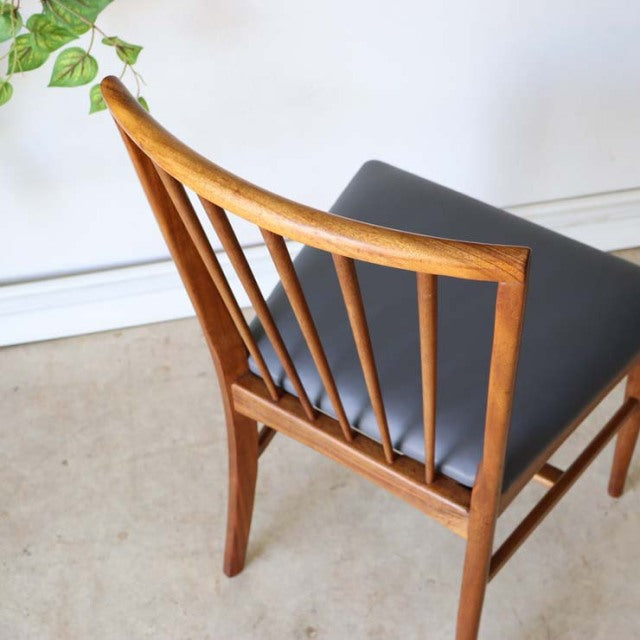 Mid-century vintage British teak dining chair with sleek tapered legs and vertical spindle backrest, black leather seat.