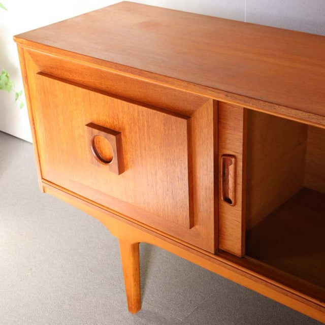 Mid-century British vintage teak sideboard with smooth wood grain, sculpted legs, and geometric door handles.