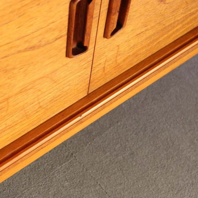 Mid-century British vintage teak sideboard corner showing warm wood grain and rounded recessed handles on clean-lined doors.