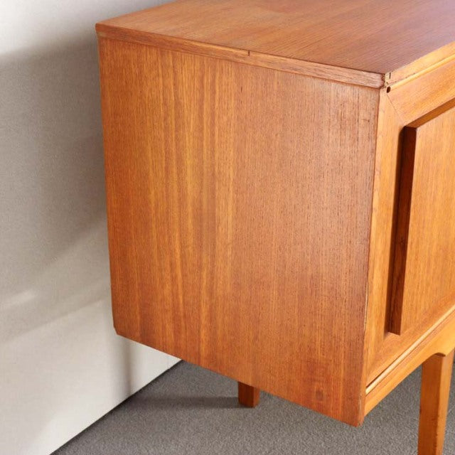 Vintage mid-century British teak sideboard with smooth wood grain and slender tapered legs.