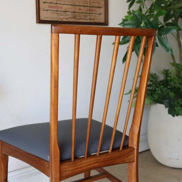 Mid-century Danish teak dining chair with slender vertical slats, warm wood grain, and black leather seat.