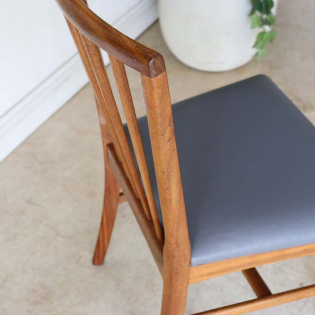 Vintage teak dining chair with sleek sharp backrest, mid-century British design, smooth wood grain, gray upholstered seat.