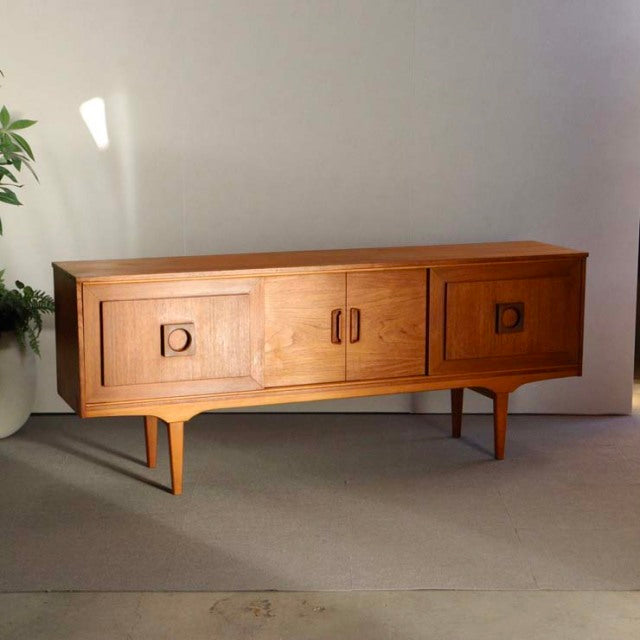Mid-century British vintage teak sideboard with smooth wood grain, square recessed handles, and tapered legs.