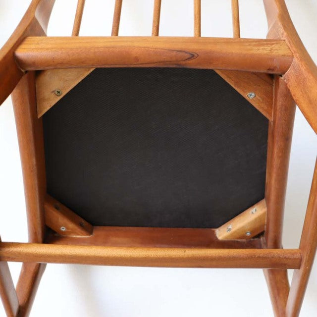 Vintage mid-century British teak dining chair viewed from below, showing warm wood grain, sturdy legs, and black upholstered .