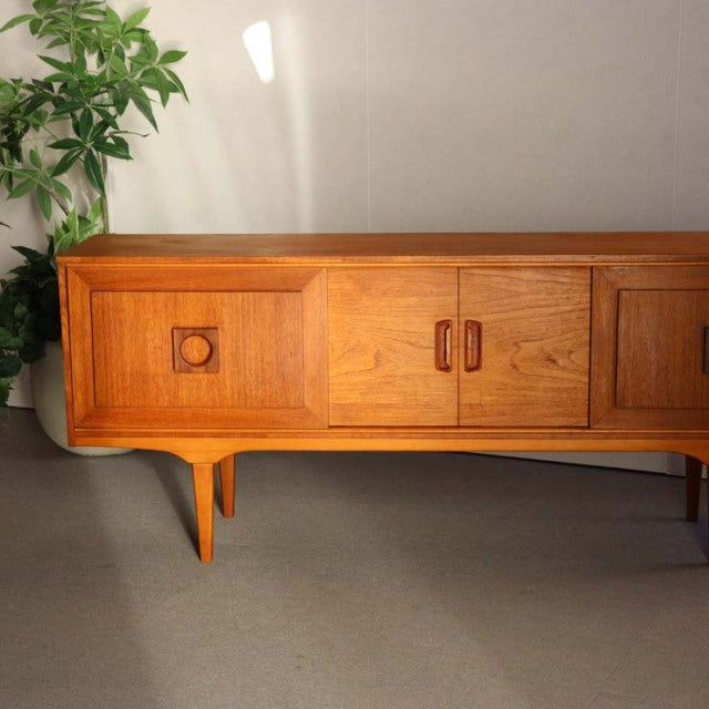 Mid-century British vintage teak sideboard with sculpted legs, central double doors, and geometric wood grain panels.