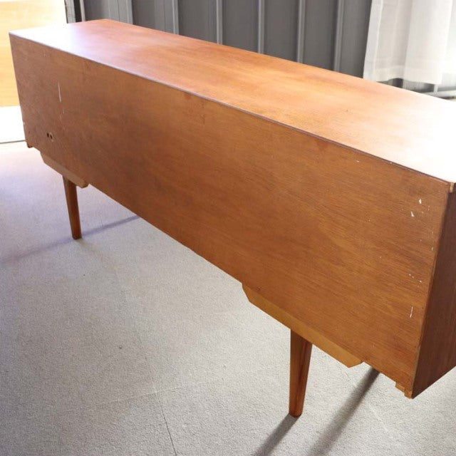 Mid-century British vintage teak sideboard with sleek wood grain, slender tapered legs, and minimalist design from Denmark.