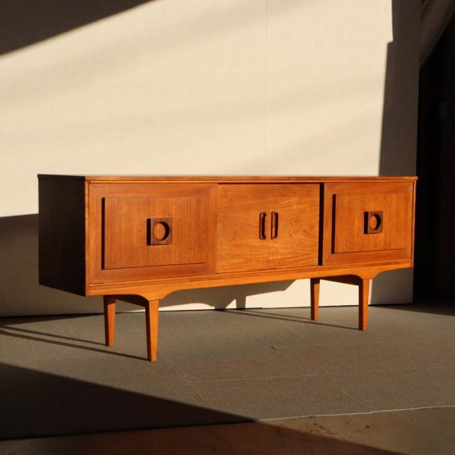 Mid-century British vintage teak sideboard with rich wood grain, rounded edges, and tapered legs.