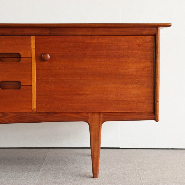 Vintage teak sideboard with smooth wood grain, rounded drawer handles, and tapered mid-century British legs.