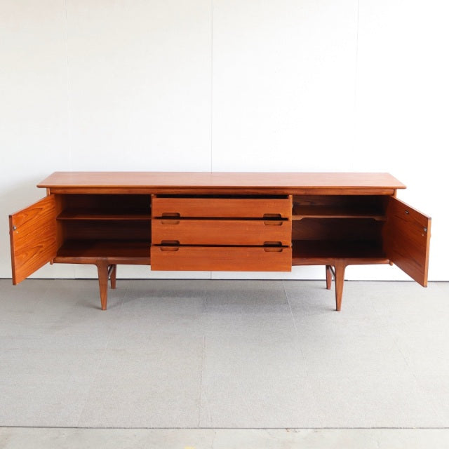 Mid-century British vintage teak sideboard by YOUNGER with rich wood grain, three drawers, and two open side cabinets on.
