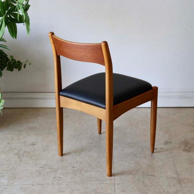 Vintage mid-century British teak dining chair with smooth wood grain and black cushioned seat, tapered legs.