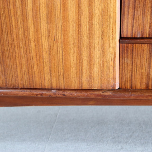 Close-up of vintage teak sideboard showing rich wood grain, smooth mid-century British design, and detailed joinery on lower .