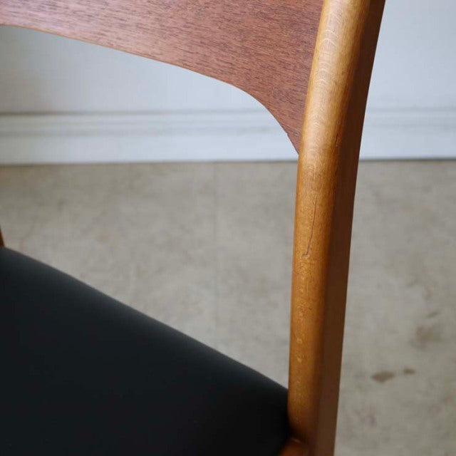 Mid-century British vintage teak dining chair with smooth curved backrest and black leather seat, showcasing warm wood grain .