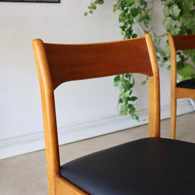 Vintage British mid-century teak dining chair with curved backrest and black cushioned seat, sleek wooden legs showing warm.