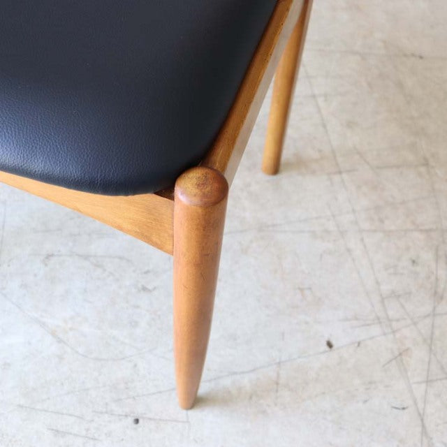 Close-up of vintage British mid-century teak dining chair leg with smooth wood grain and black leather seat.