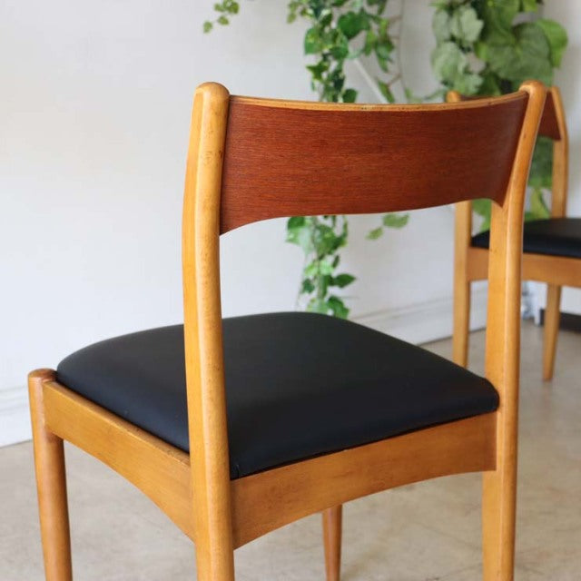 Mid-century British vintage teak dining chair with black leather seat, curved backrest, and tapered legs.