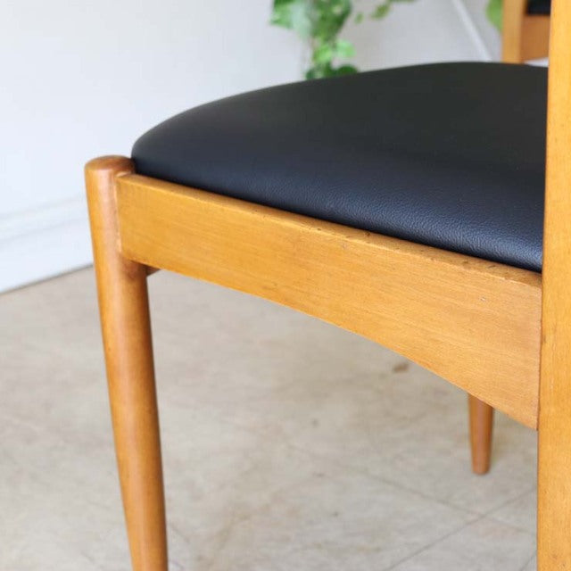 Mid-century British vintage teak dining chair with smooth wood grain, tapered legs, and black leather seat from Denmark.