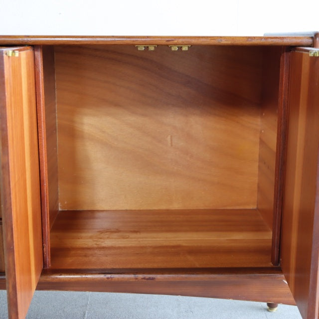 Open vintage British mid-century teak sideboard interior showing smooth wood grain and brass hinges.