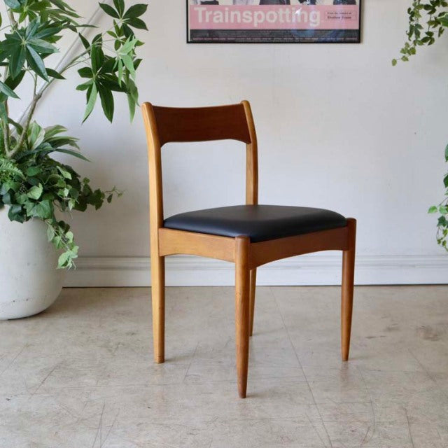 Mid-century British vintage teak dining chair with sleek black cushioned seat and tapered legs.