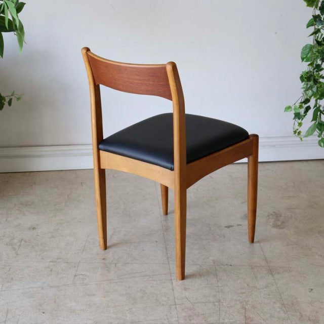 Vintage teak dining chair with black upholstered seat, sleek mid-century British design, gently curved backrest and tapered.