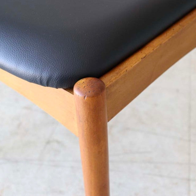 Vintage teak dining chair corner with smooth wood grain, rounded leg joint, and black mid-century seat upholstery from.