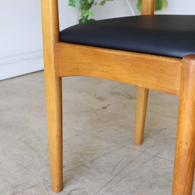 Vintage teak dining chair with smooth black seat, slender tapered legs, mid-century British Denmark design, natural wood.