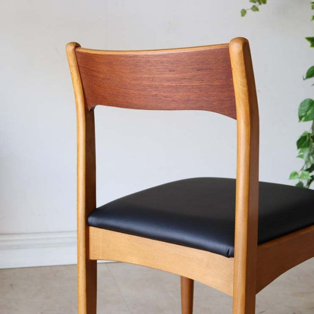 Vintage mid-century teak dining chair with black leather seat, curved wood grain backrest, and slender rounded legs from.