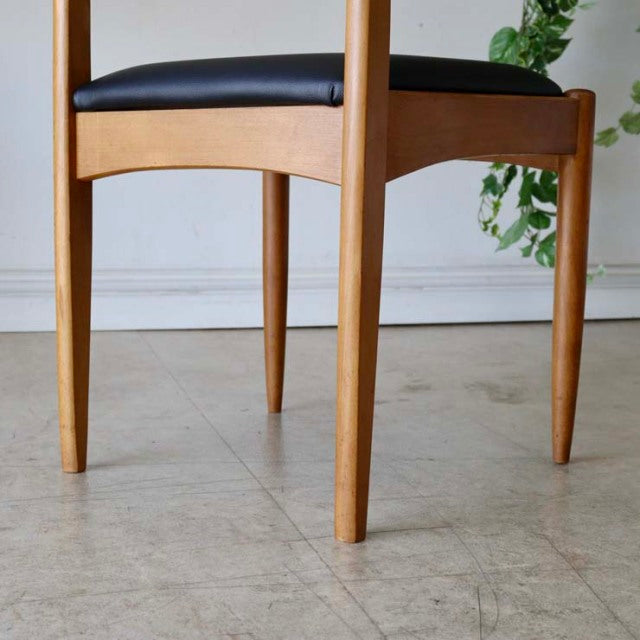 Pair of vintage teak dining chairs with sleek black leather seats, slender tapered legs, and smooth mid-century.