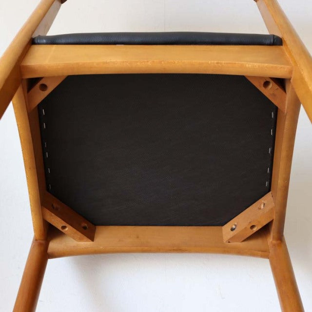 Vintage teak dining chair viewed from below, showcasing natural wood grain, sturdy angled legs, and black upholstered seat.