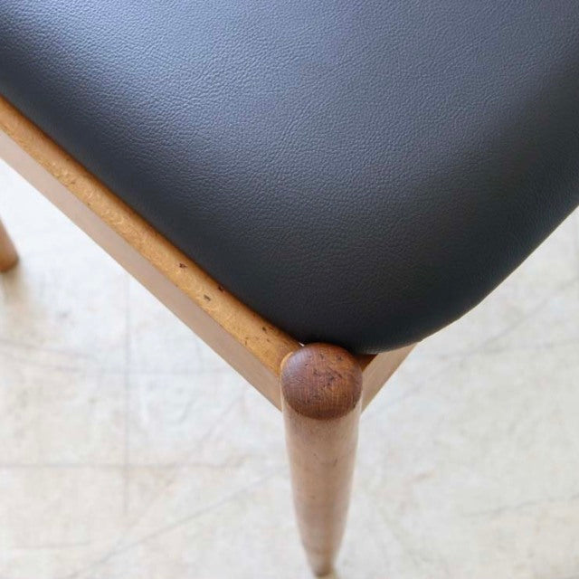 Close-up of vintage British teak dining chair corner with smooth black seat and tapered wooden leg showing mid-century.