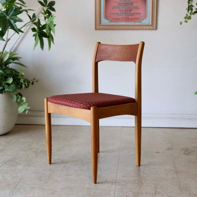 Vintage teak dining chair with mid-century British design, red floral seat cushion, slender angled legs, smooth wood grain.