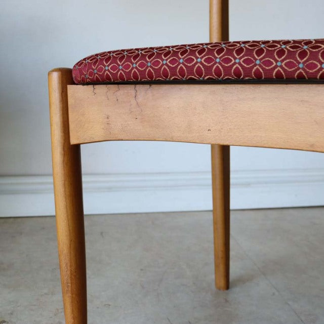 Mid-century vintage British teak dining chair with tapered legs and red floral patterned seat cushion.