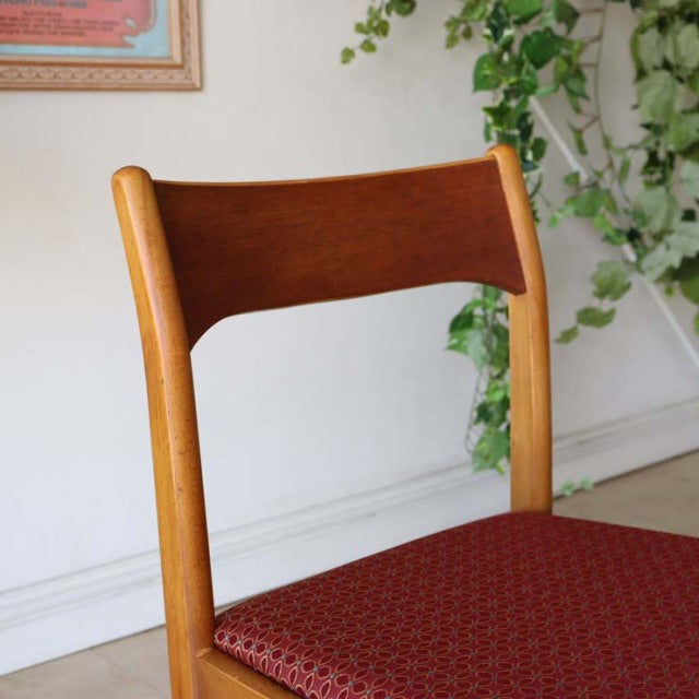 Vintage British mid-century teak dining chair with curved backrest and red patterned flower seat cushion, smooth wood grain.
