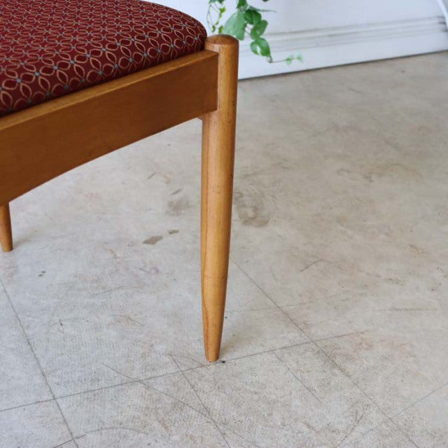 Mid-century British vintage teak dining chair leg with smooth wood grain and tapered design, flower-patterned red seat fabric.