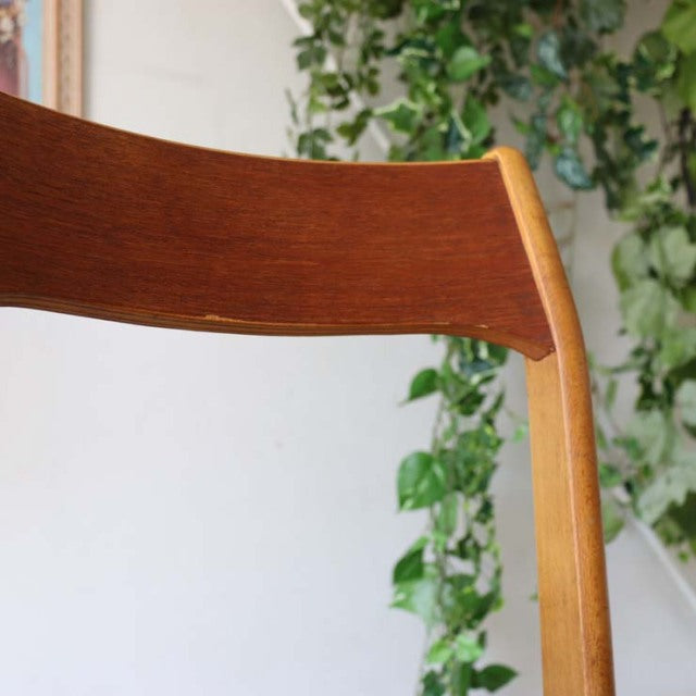 Close-up of vintage teak mid-century British dining chair showing curved backrest with rich wood grain and smooth light wood .